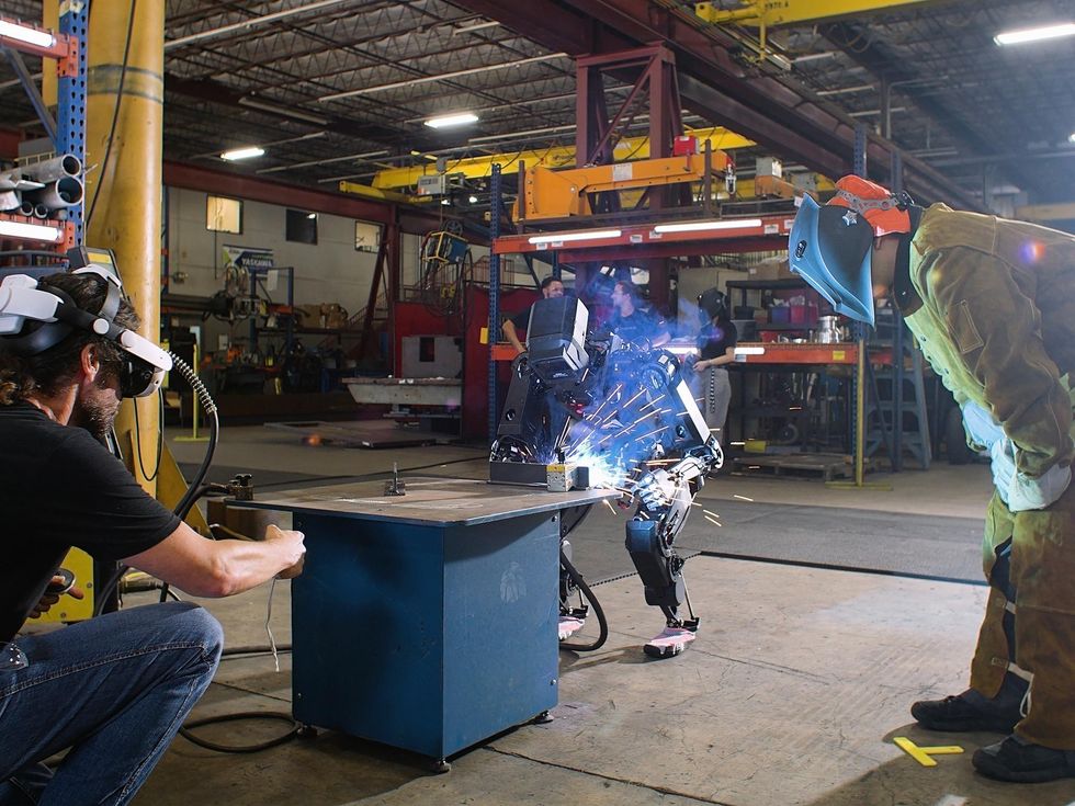 Engineers supervising a humanoid robot performing an industrial welding task
